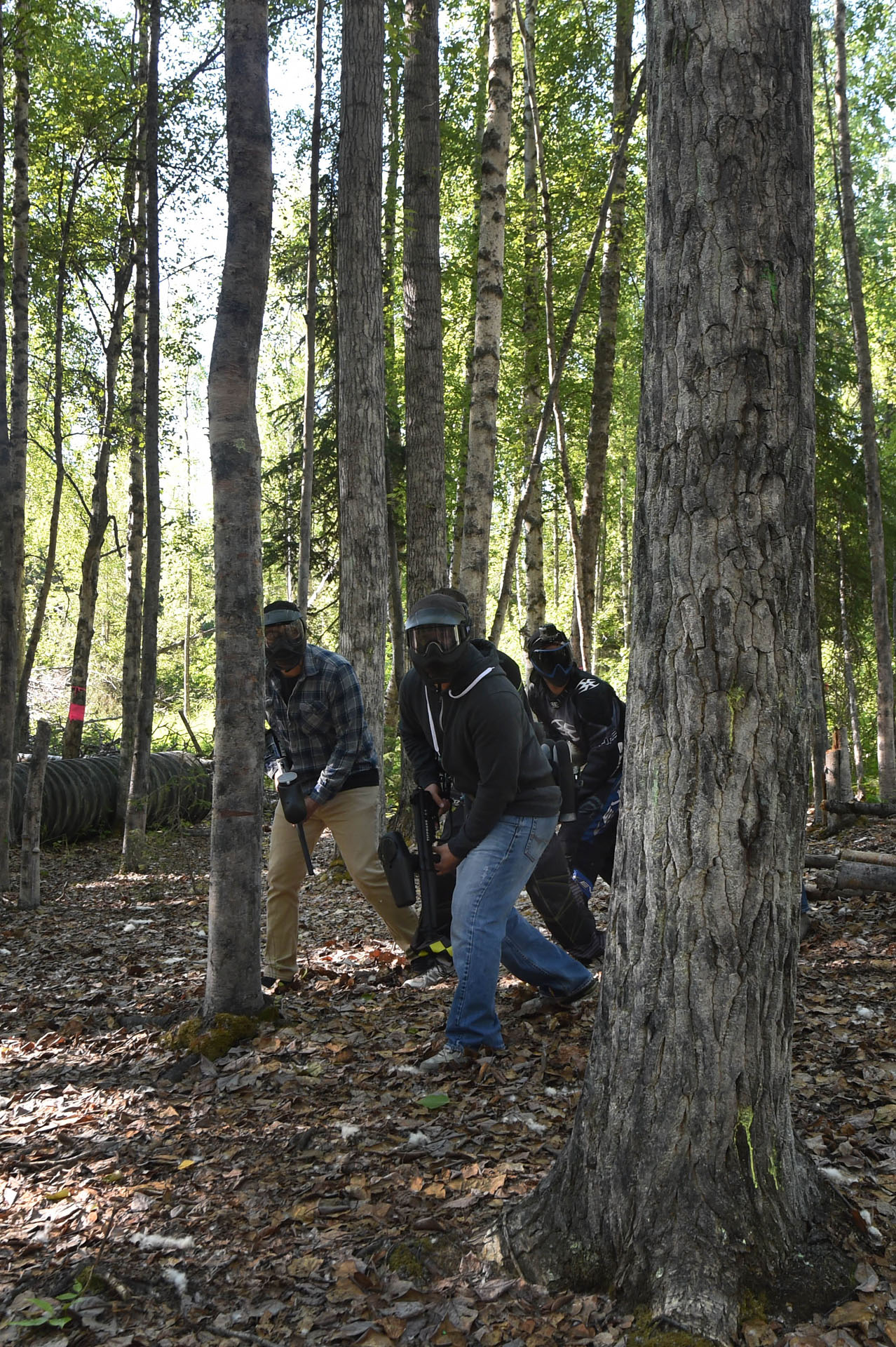 A group of paintball players moving together behind a tree